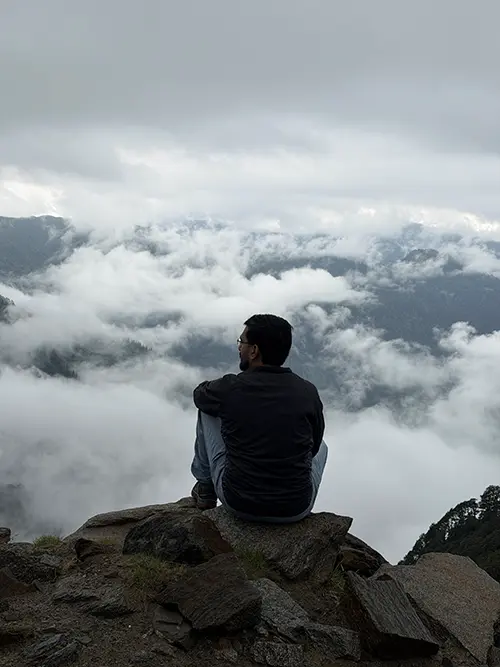 Dr. Yashasvi Verma seated on a rock overlooking a cloudy mountain valley