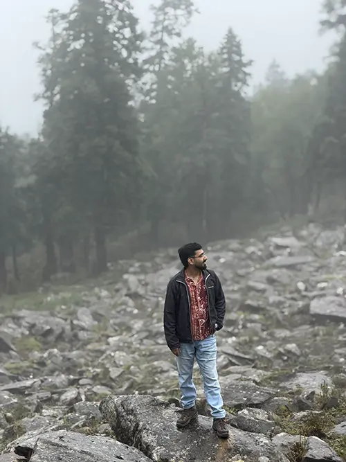 Dr. Yashasvi Verma standing on rocky ground in a forested landscape